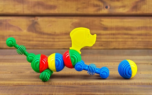 Toy dog made from plastic colorful details and ball on wooden background