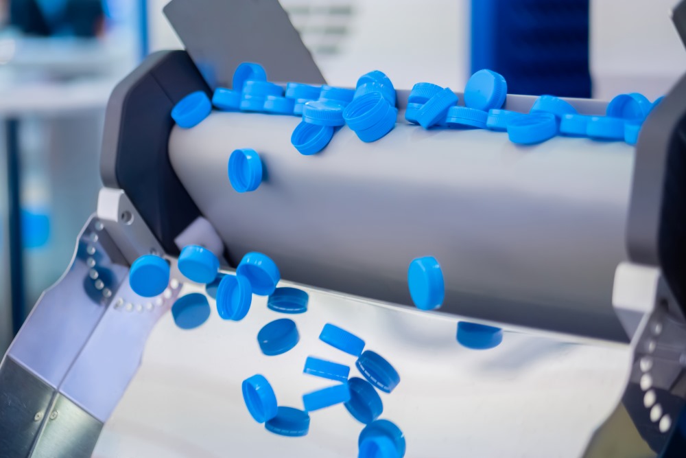 Injection molding production line - many blue plastic bottle caps falling from conveyor belt at factory, exhibition.